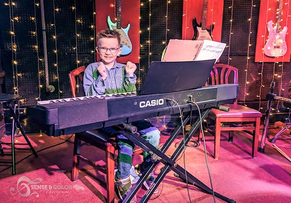 student smiles while sitting at a piano on stage