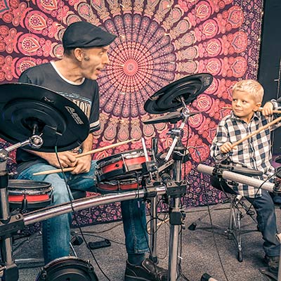 drum teacher plays on drum set with young student