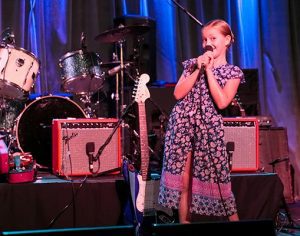 girl smiles while singing on stage