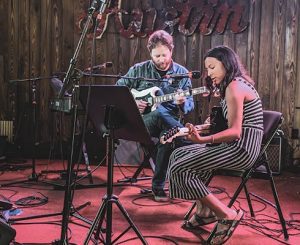 Male teacher on stage with female student on guitar