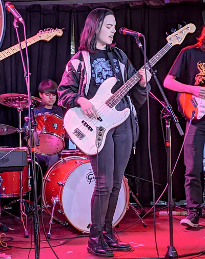 Teenage girl plays bass guitar on stage with a rock band