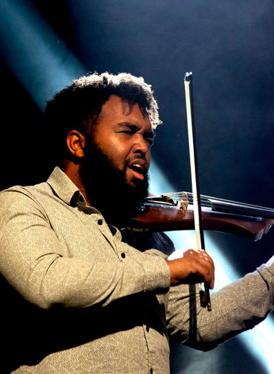 Black man plays violin on stage with concert lighting