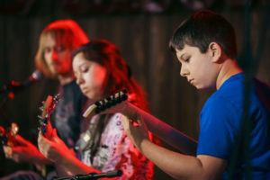 brother and sister play guitar and bass with music teacher on stage