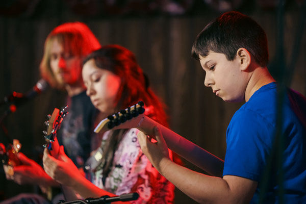 brother and sister play guitar and bass with music teacher on stage