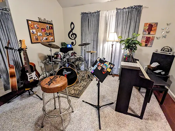 music lesson room with drum set, acoustic guitars, upright piano, stool, and music stand