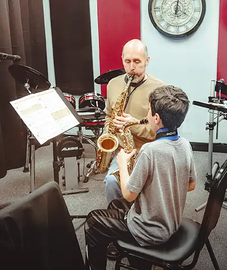 Teacher and student play saxophones in music school