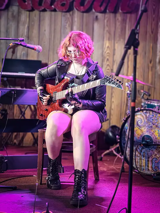 Female guitar student plays electric guitar on stage