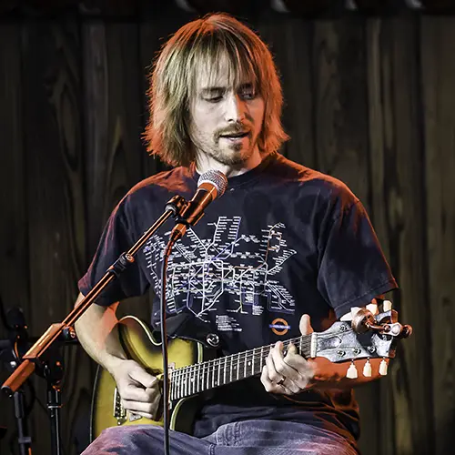 Male bass and guitar teacher with long hair plays electric guitar on stage