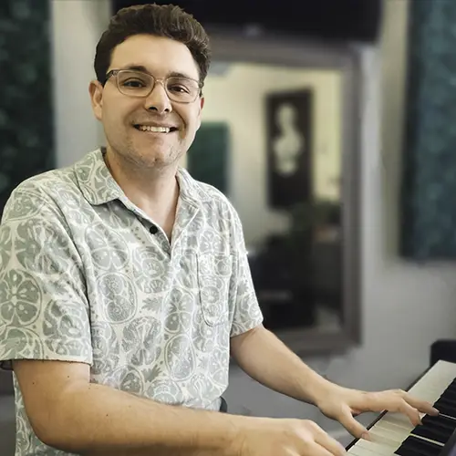 Male piano teacher sitting at upright electric piano smiles at the camera