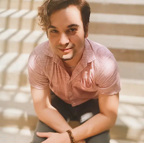 Male voice and piano teacher with dark hair sits on steps, looking toward camera