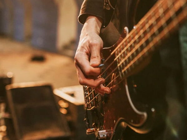closeup of man's hand playing a bass guitar on stage with drums in the background