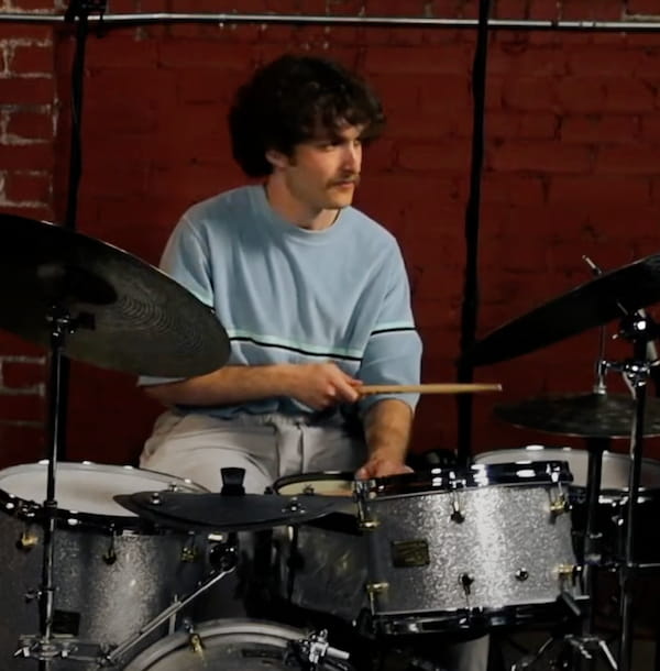 Young male drummer with dark curly hair sits at drum kit, holding drum sticks